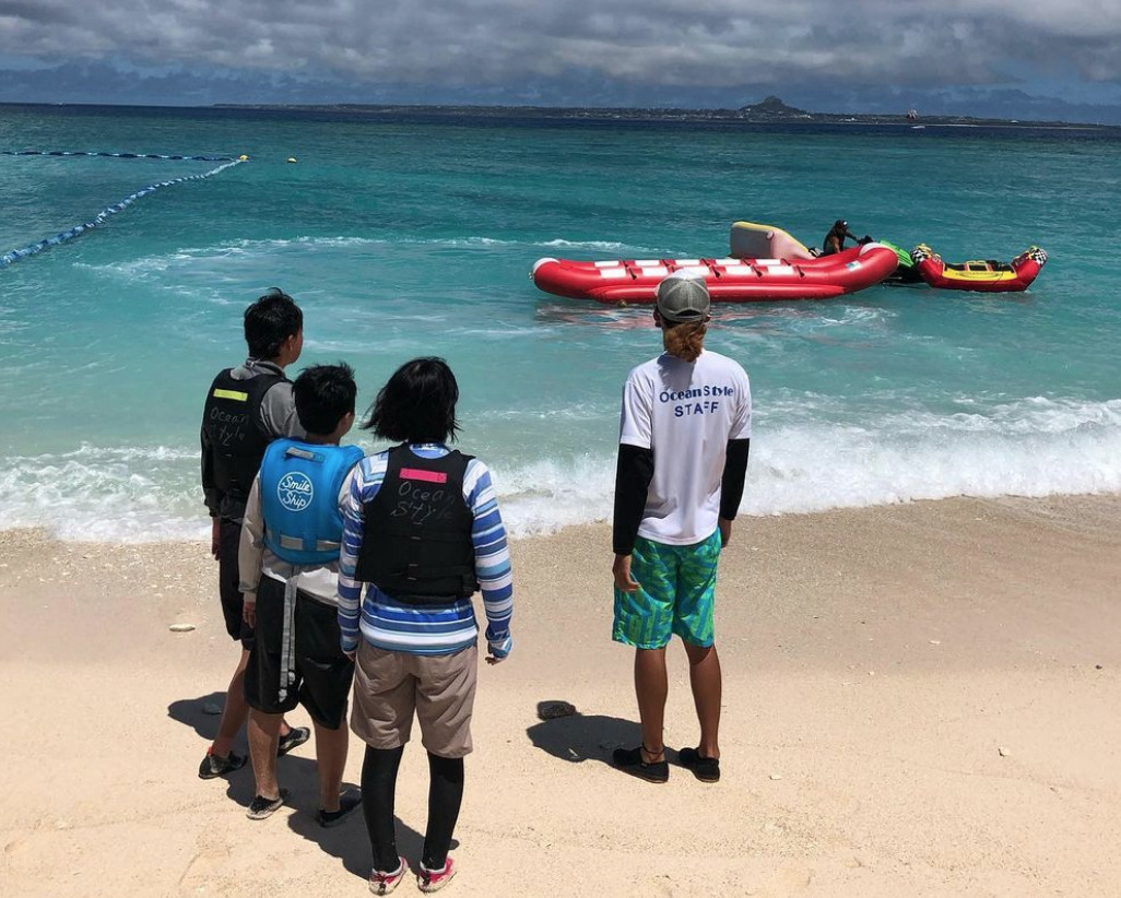 水納島マリンスポーツの講習。砂浜でバナナボートを前に説明を聞く3人の参加者