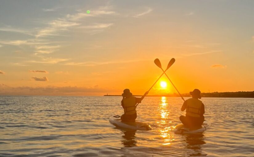 伊江岛，日落时分，一对情侣站在SUP板上高举桨板合影留念