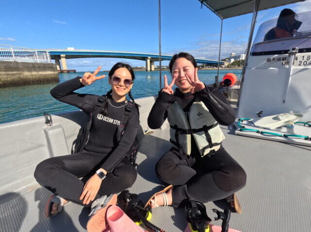 水納島マリンスポーツのダイビング船上。機材を前にピースサインをする女性客