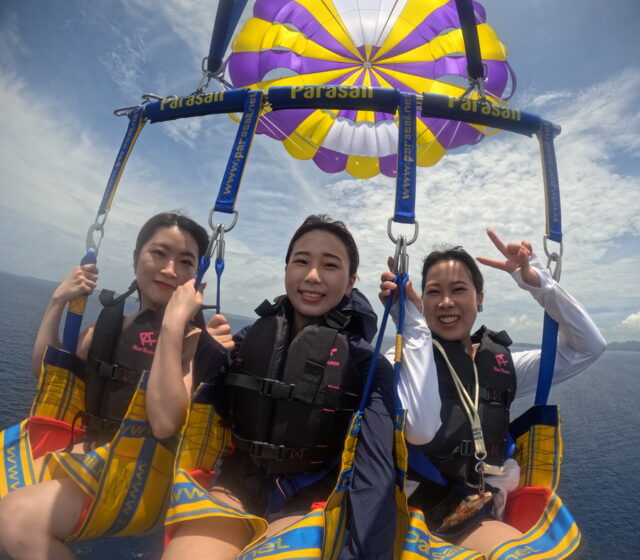 水納島の上空を楽しむパラセーリング体験中の女性3人