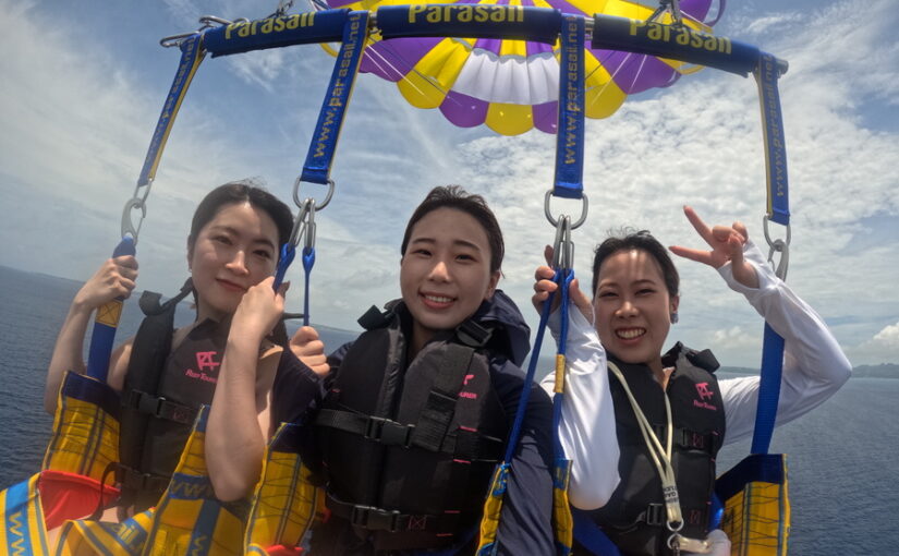 水納島の空でパラセーリングを楽しむ3人の女性
